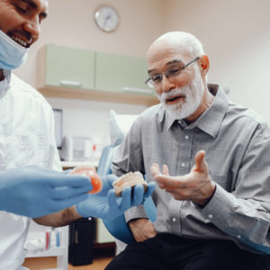 Oudere man met baard overweegt om een kroon of brug te plaatsen samen met de tandarts