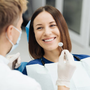 Vrouw in een blauw shirt krijgt uitleg van een tandarts voor een gebitsprothese.