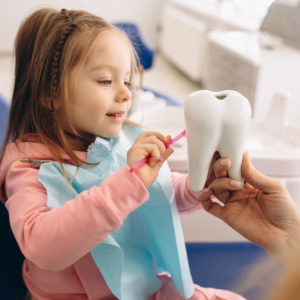 Kind met een blauw doekje en een tandenborstel in haar hand probeert een grote tand te poetsen