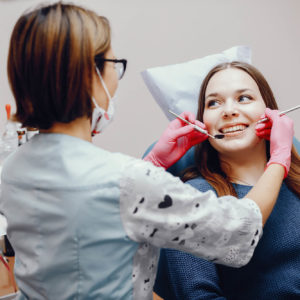 Vrouw in een blauwe trui wordt door de tandarts met bril geholpen aan haar Tand- of kiespijn
