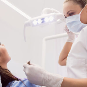 Vrouw in een blauw shirt komt op controle afspraak bij de tandarts met blonde haren en in het wit gekleed